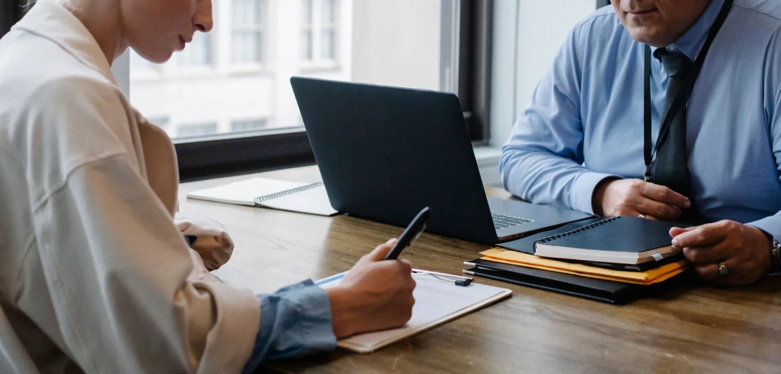 Twee professionals bespreken documenten aan een bureau met laptop en notitieblok