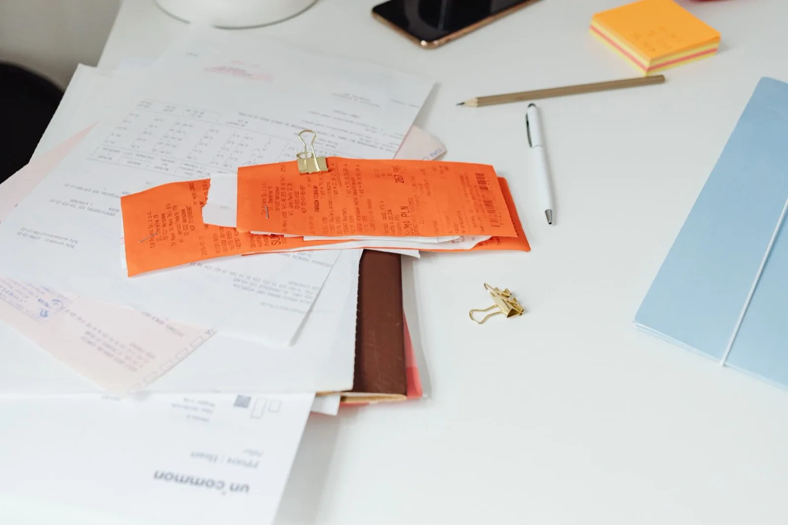Stapels bonnetjes en documenten op een bureau, met pen en memoblaadjes