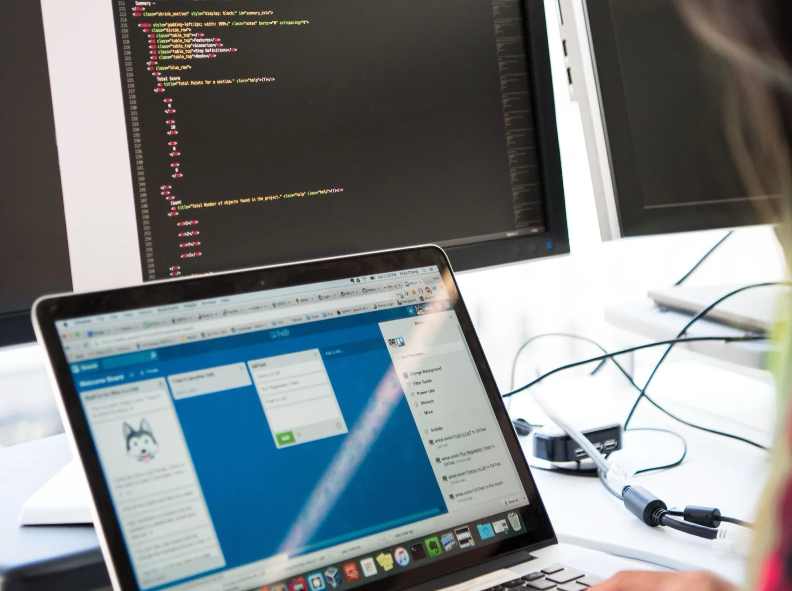 Programmeur achter twee beeldschermen met code en een projectbord